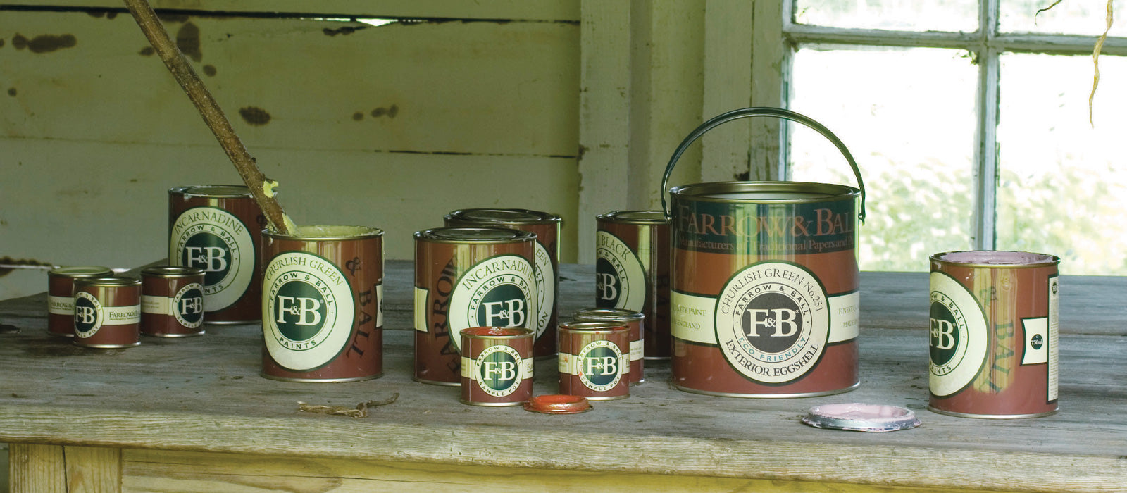 Mehrere rote Farrow and Ball Farbdose in unterschiedlichen Größen auf einem alten Tisch in einer Scheune positioniert