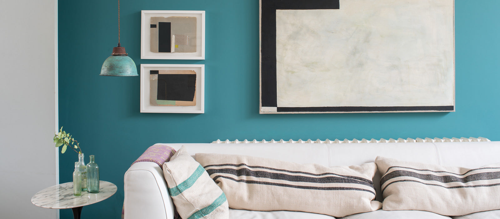 Ein Wohnzimmer mit einer türkisen Wand, davor ein weißes Sofa und schwarz graue Bilder an der Wand als Akzente