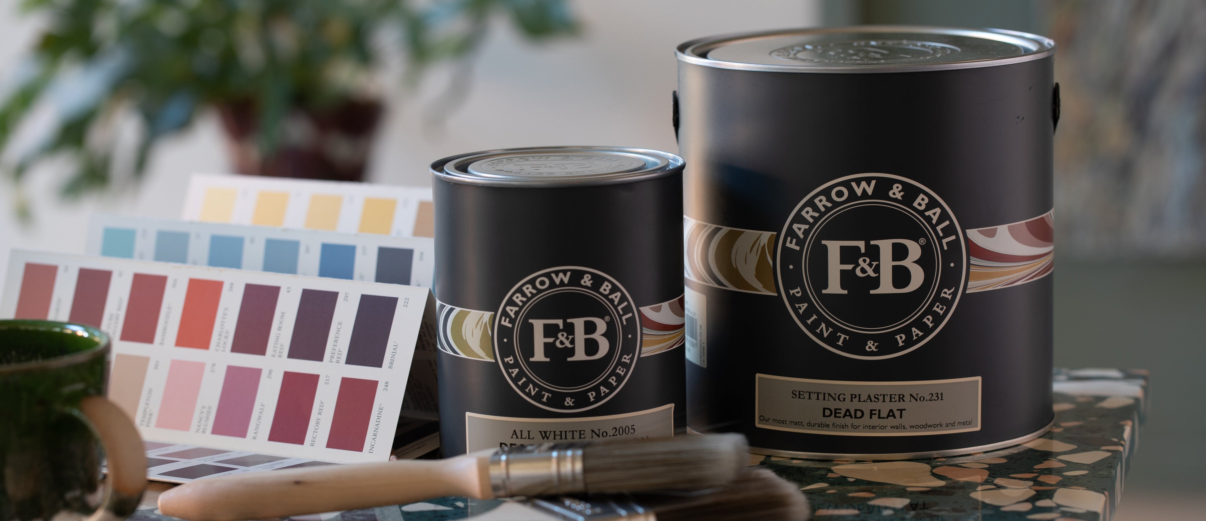Zwei Farbdosen von Farrow & Ball als Dead Flat mit einer Farbkarte daneben und einem Pinsel davor